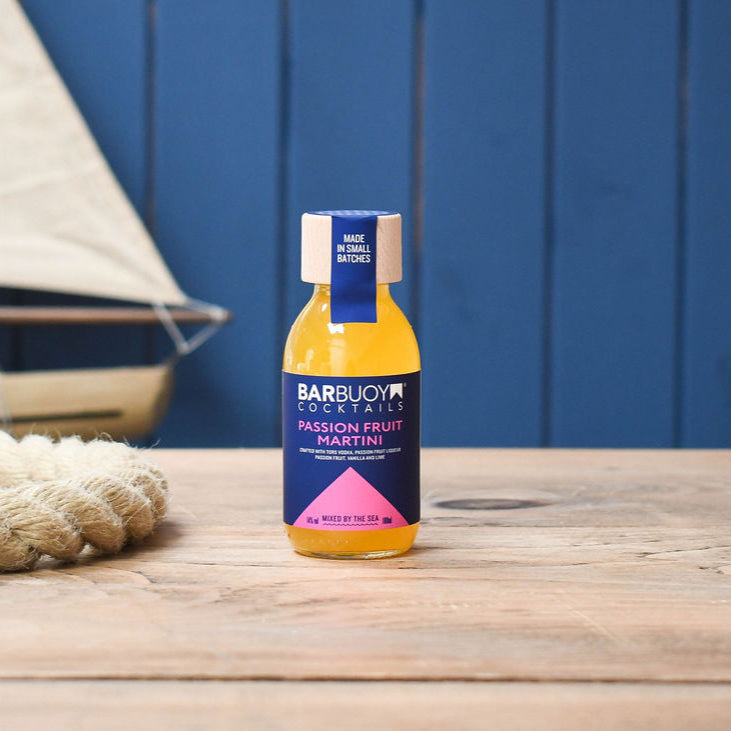Bottle of Bar Buoy Passion Fruit Martini cocktail on a wooden surface with a blue background
