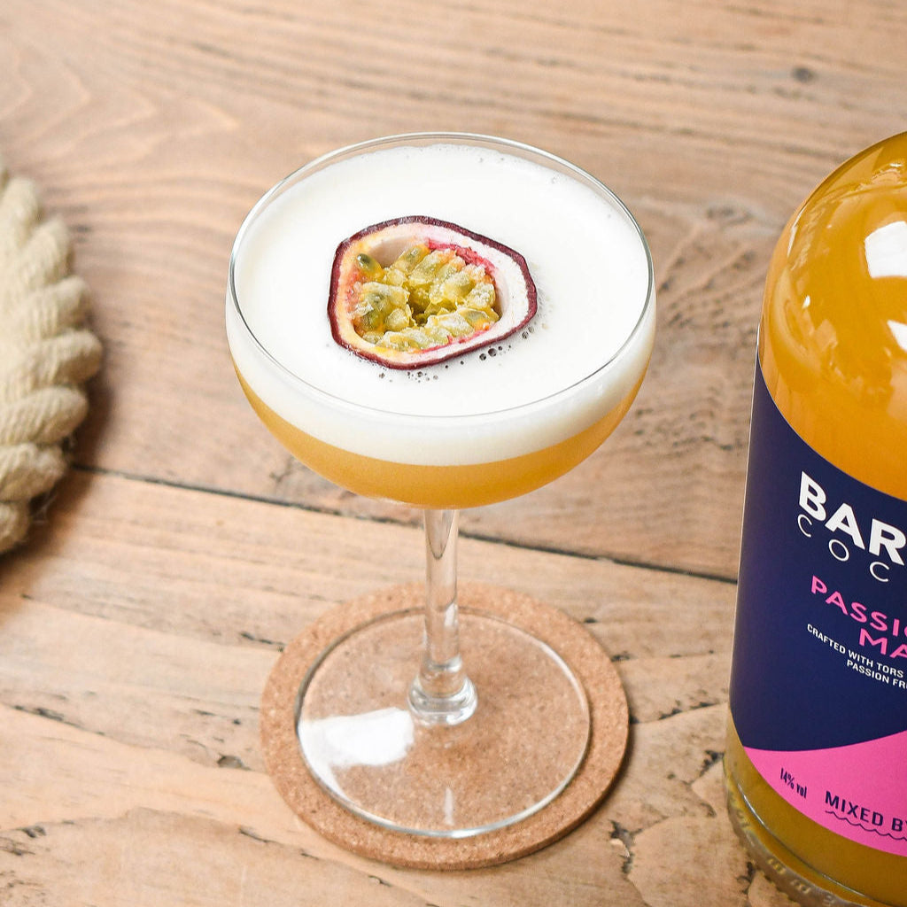 Cocktail with a passion fruit martini next to a bottle of Bar Buoy cocktail on a wooden surface.