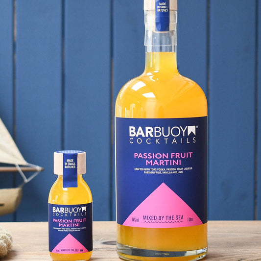 Bar Buoy Cocktails Passion Fruit Martini large bottle and small bottle on a wooden surface with a blue background.