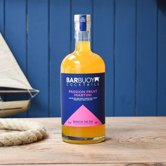 Barbuoy Cocktails Passion Fruit Martini bottle on a wooden surface with a blue background and sailboat.