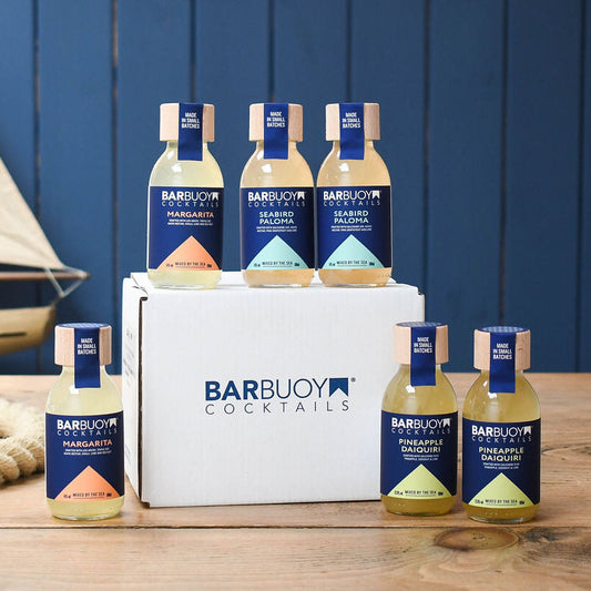 Barbuoy Cocktails bottles and packaging on a wooden surface with a blue background