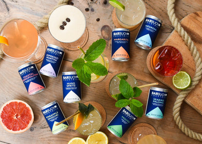 Bar Buoy cans and poured cocktails on a wooden table with citrus and mint