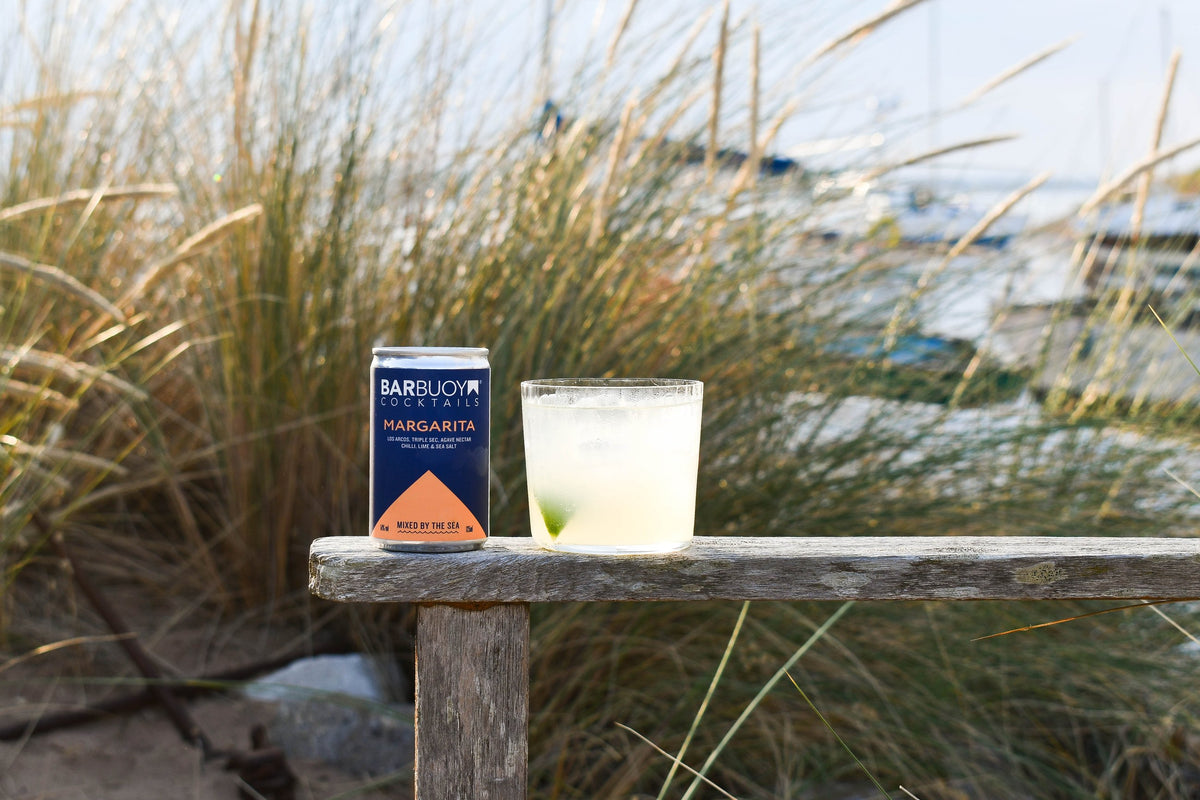 Bar Buoy Margarita can and a poured Margarita on a wooden bench in the sand dunes